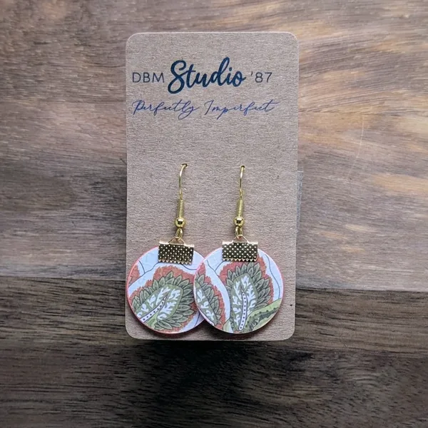 quarter size round earrings made from layers of paper modpodged together, Green, salmon and white leaves front and light and dark salmon textured back. The color of the sides made by the paper inside is salmon/pink. Gold-tone findings.